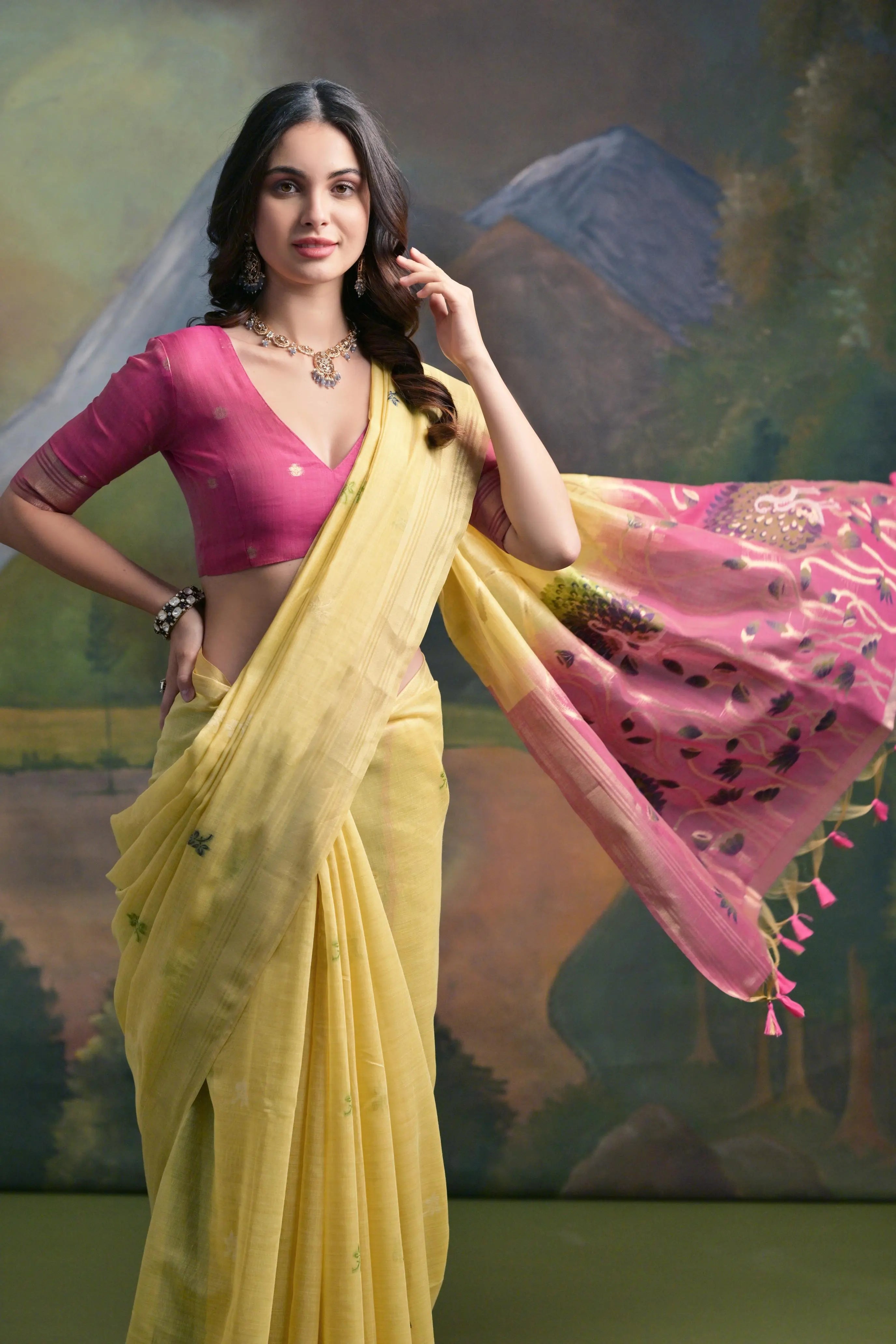 A woman models a soft Pastel Yellow Muga Silk Saree with subtle Resham weaving. The pallu dramatically transitions to a deep magenta color, featuring intricate purple and pink floral/peacock Resham threadwork. She wears a fuchsia blouse and an oxidized silver necklace.